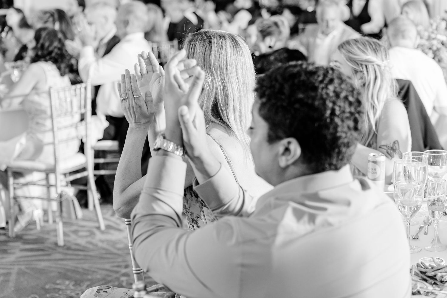 Black and white photo of guests clapping and celebrating at an elegant wedding reception banquet.