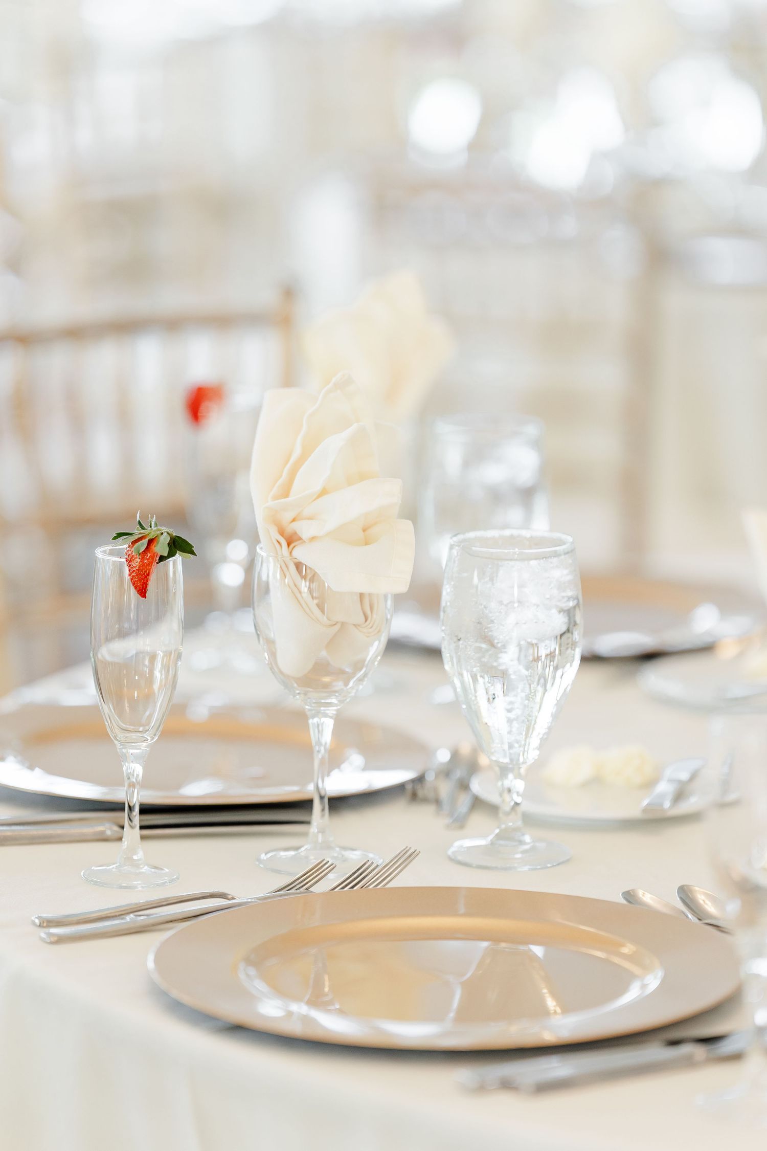Elegant wedding reception table setting with silver charger plates, crystal glassware, and cream folded napkins.