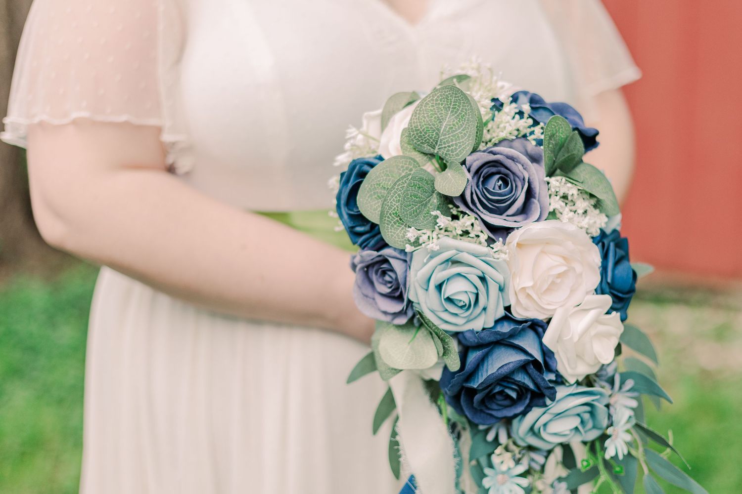 A close-up of a beautiful blue and white wedding bouquet held against a white dress.