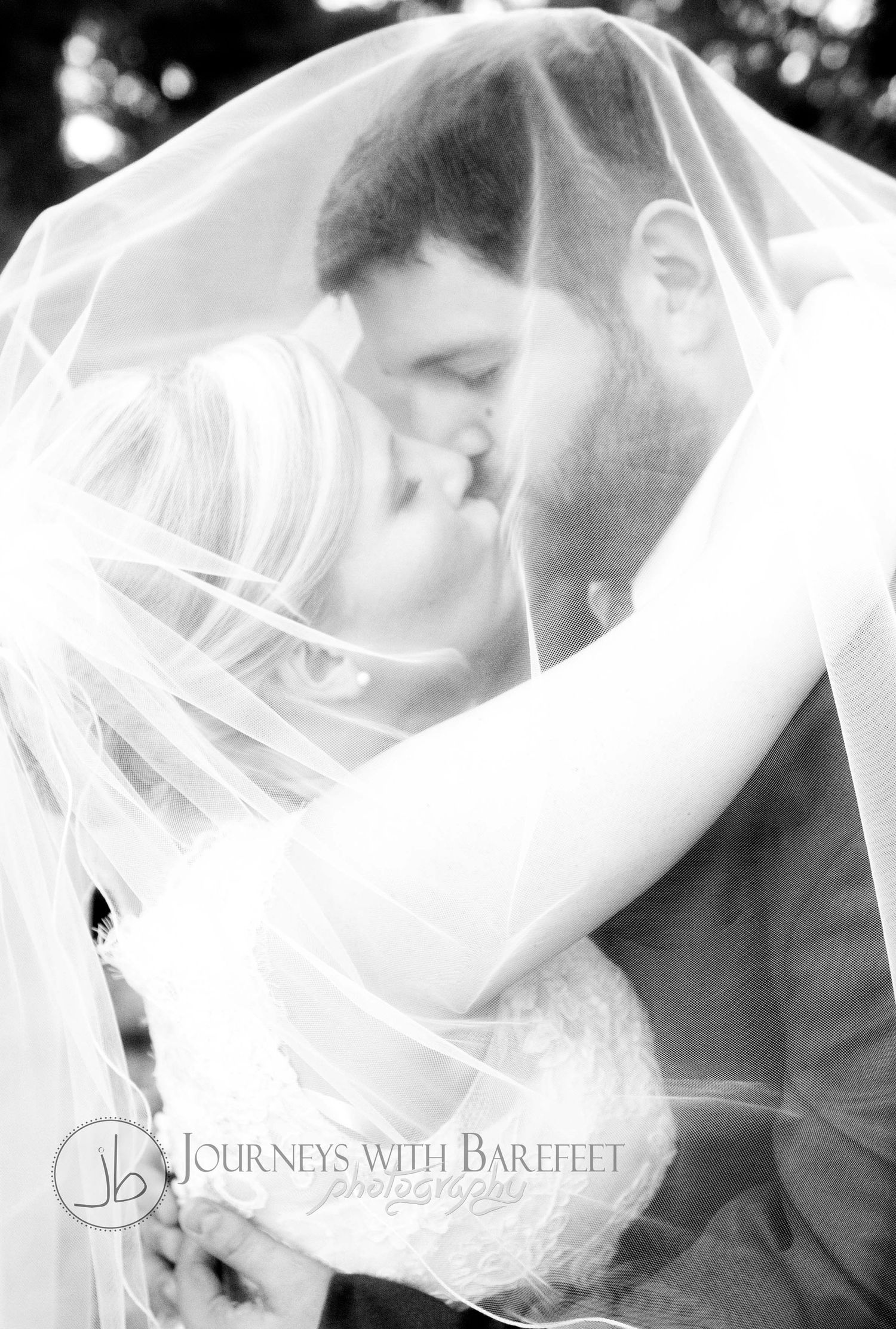 Romantic black and white portrait of couple kissing under wedding veil.