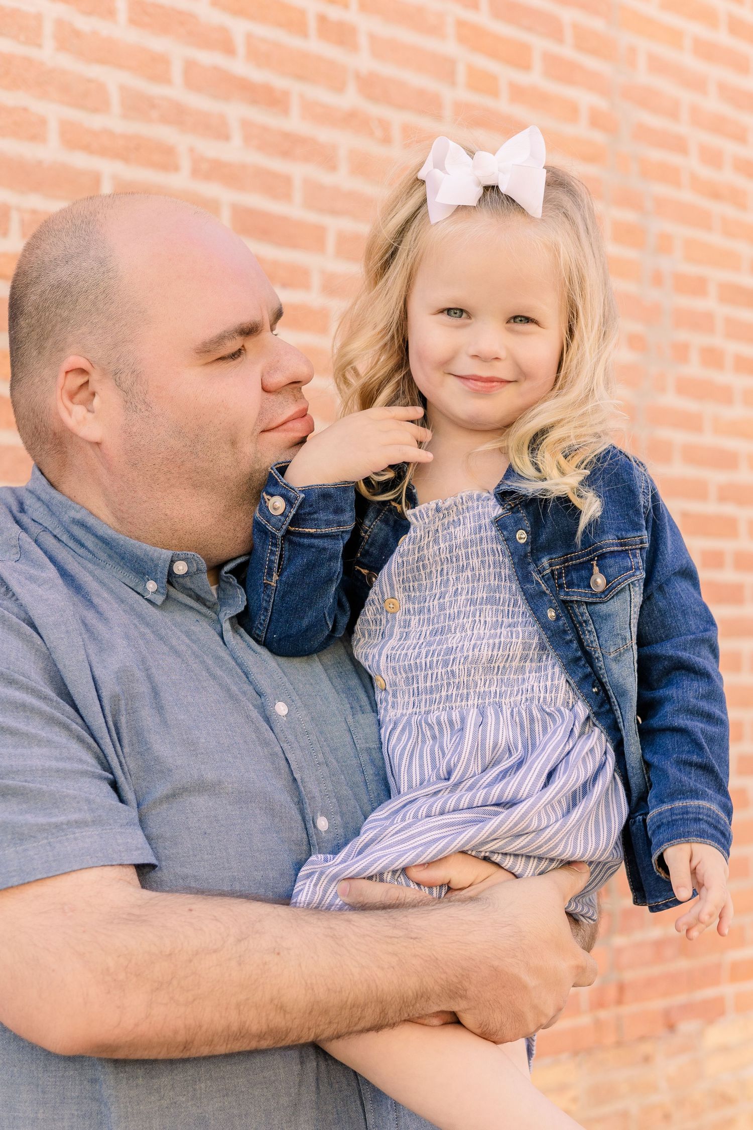 Heartwarming moment between adult and child wearing denim against brick wall backdrop.