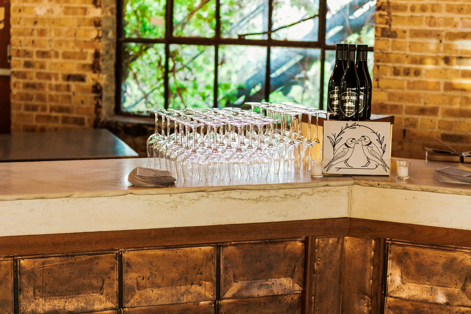 Row of crystal glasses lined up on a wooden bar with exposed brick wall backdrop.