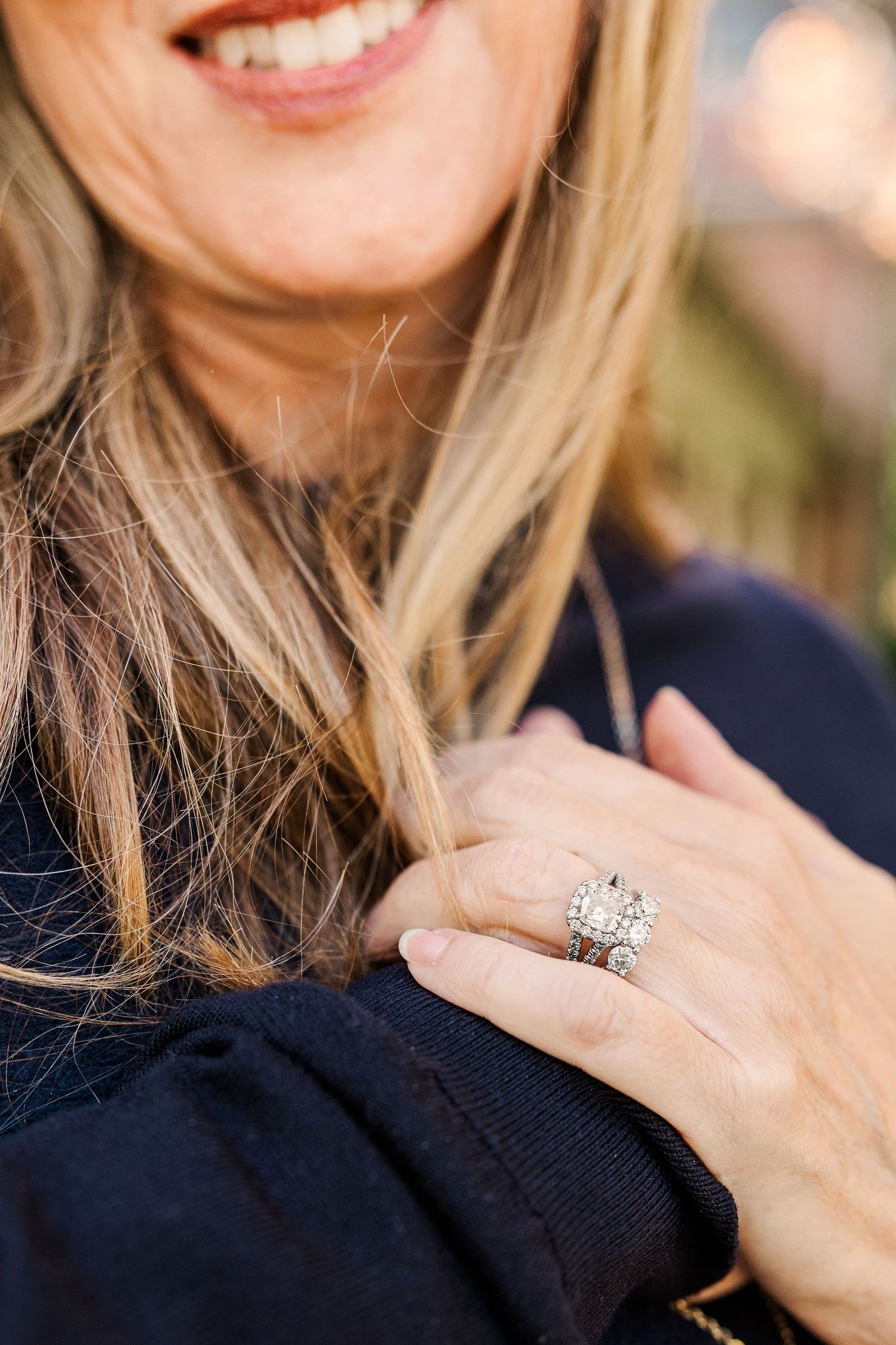 Close-up of an engagement ring sparkling on a hand against a navy blue sweater.