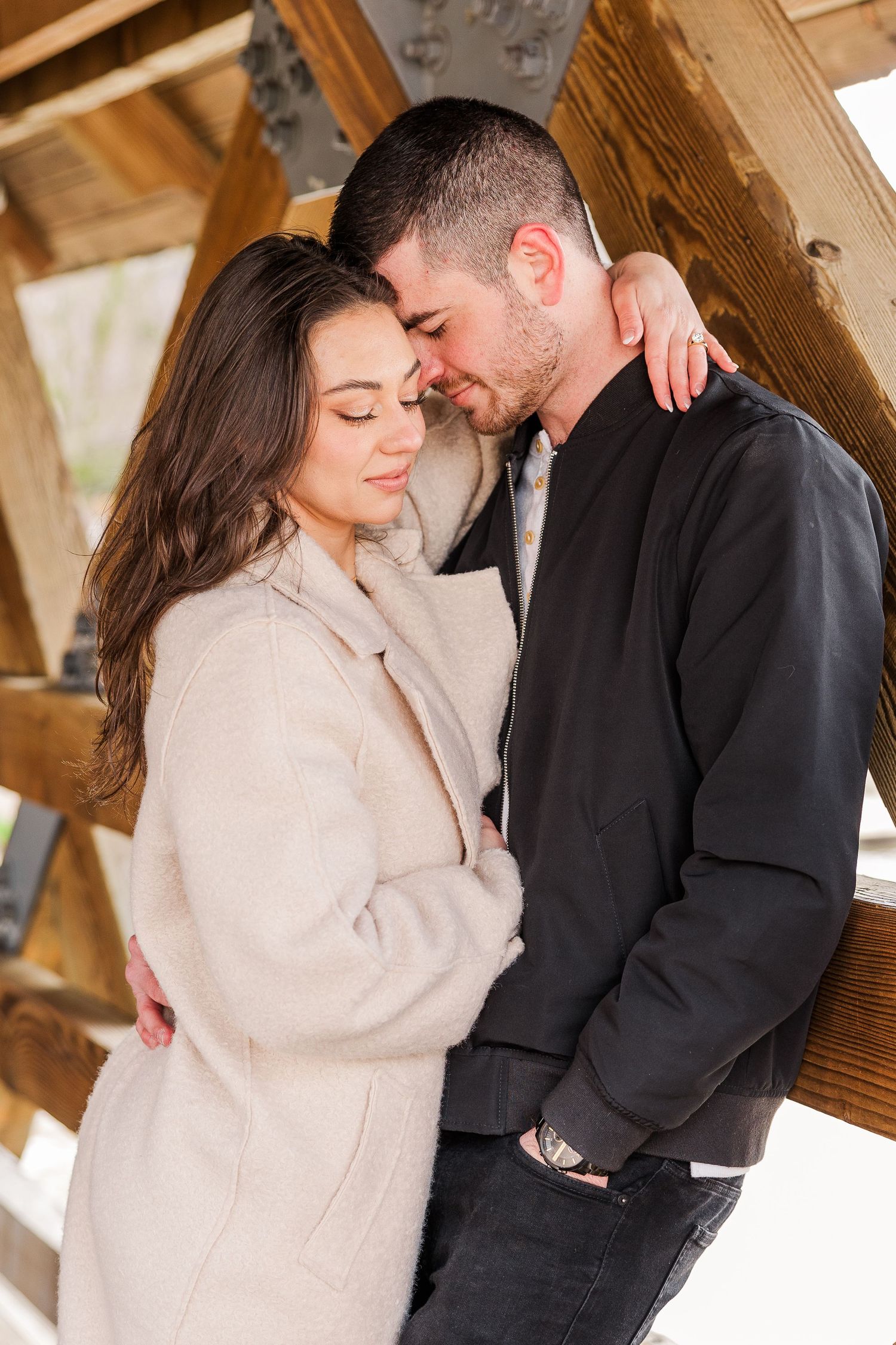 A couple in contrasting outfits sharing a tender moment in a wooden bridge setting.