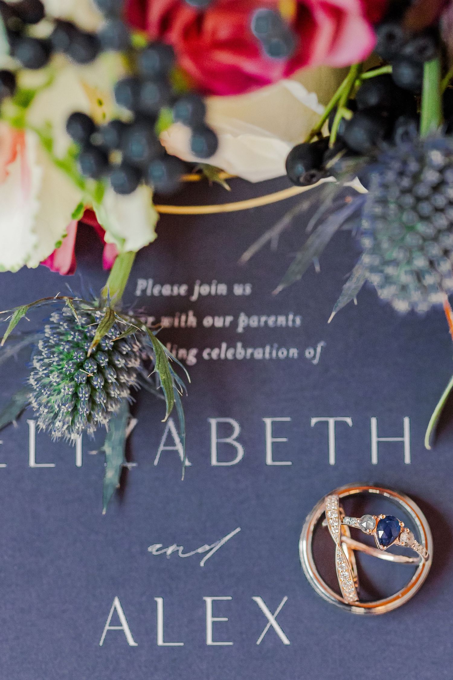 Wedding invitation for Elizabeth and Alex with floral decor and engagement ring against a dark background.