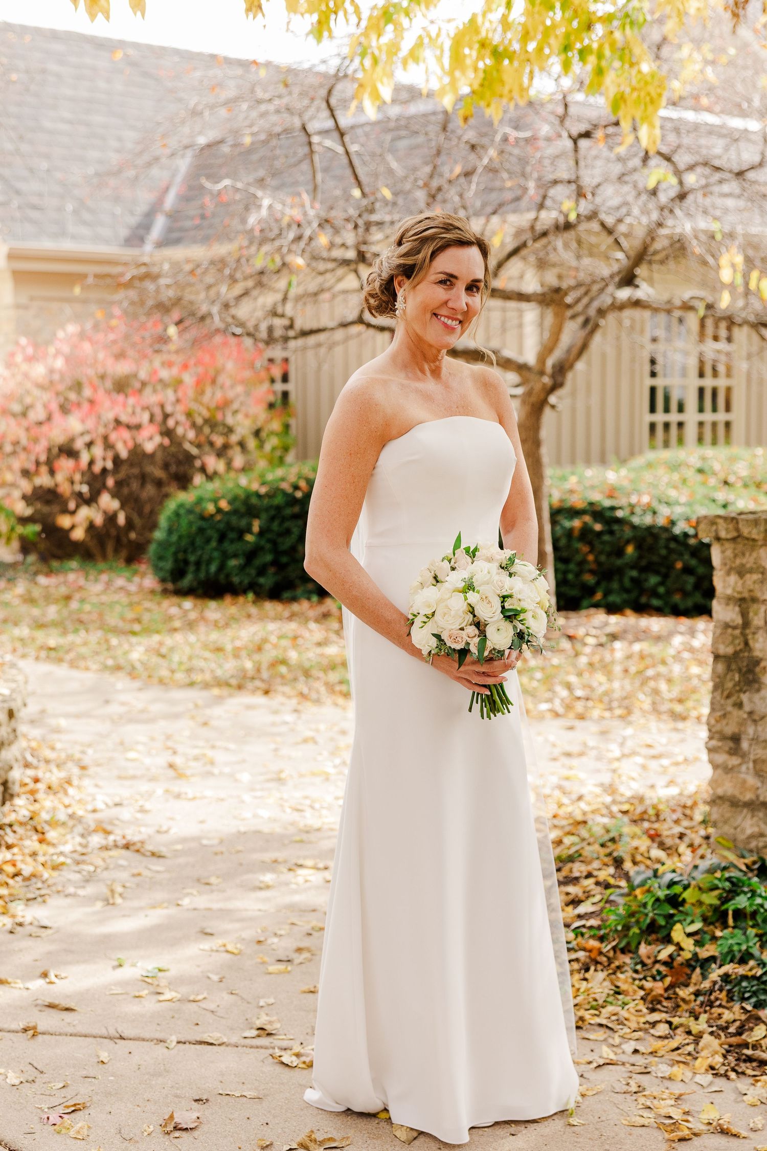 Elegant white wedding gown photographed in autumn garden setting.