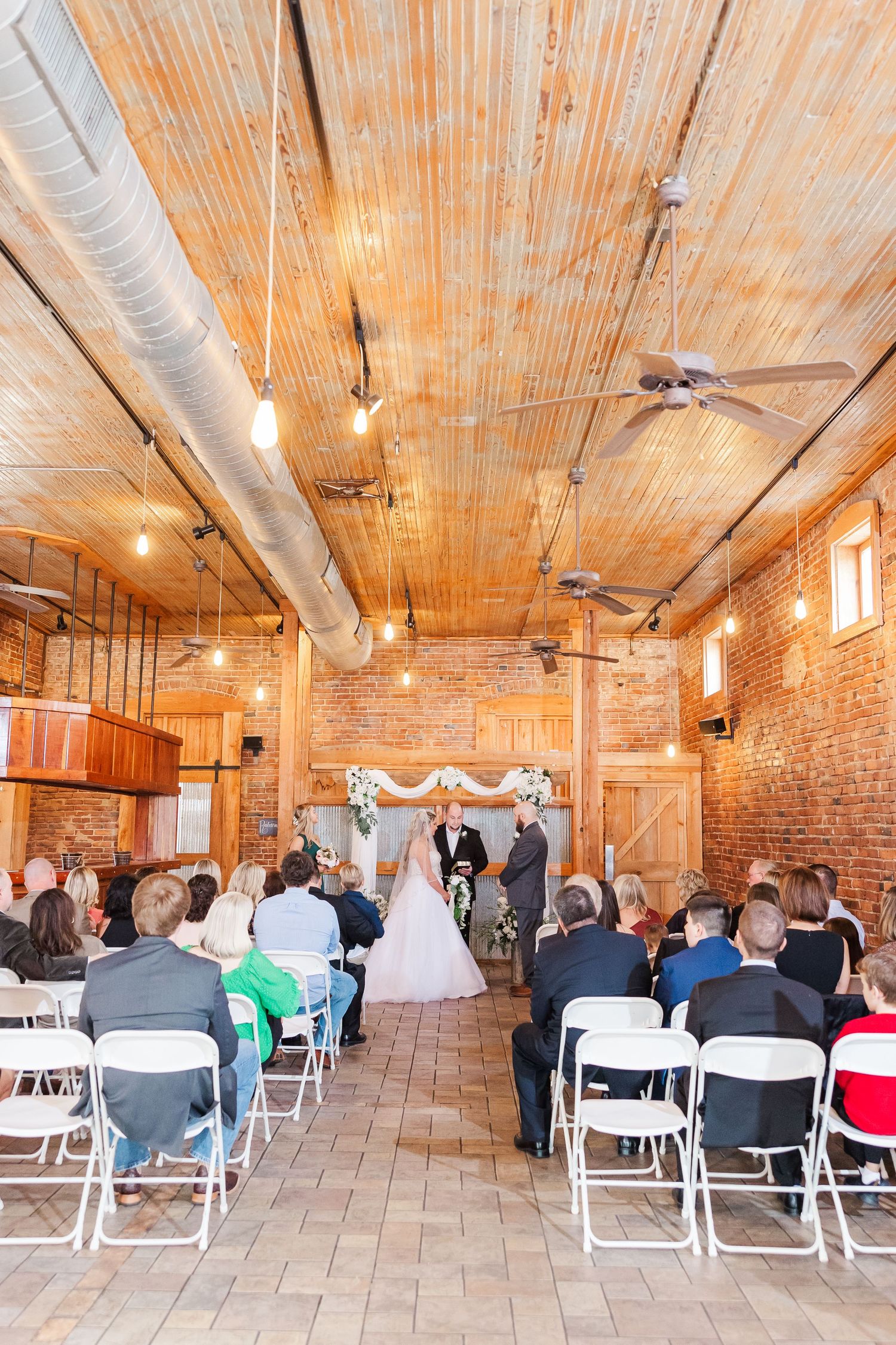 Wedding ceremony in a rustic industrial venue with exposed brick walls and wooden ceiling.