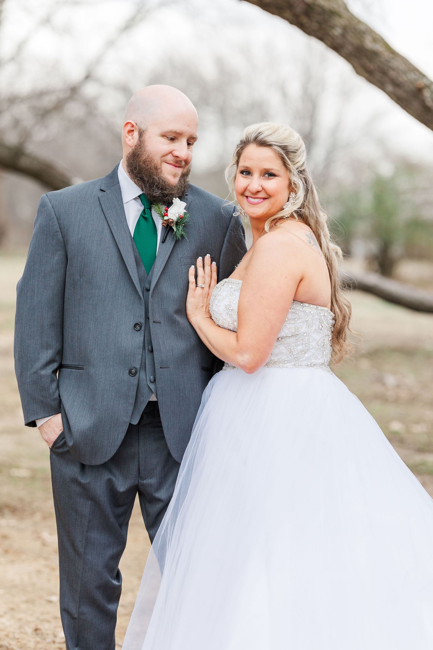 Wedding portrait featuring elegant couple in gray suit and white ballgown beneath tree branches.