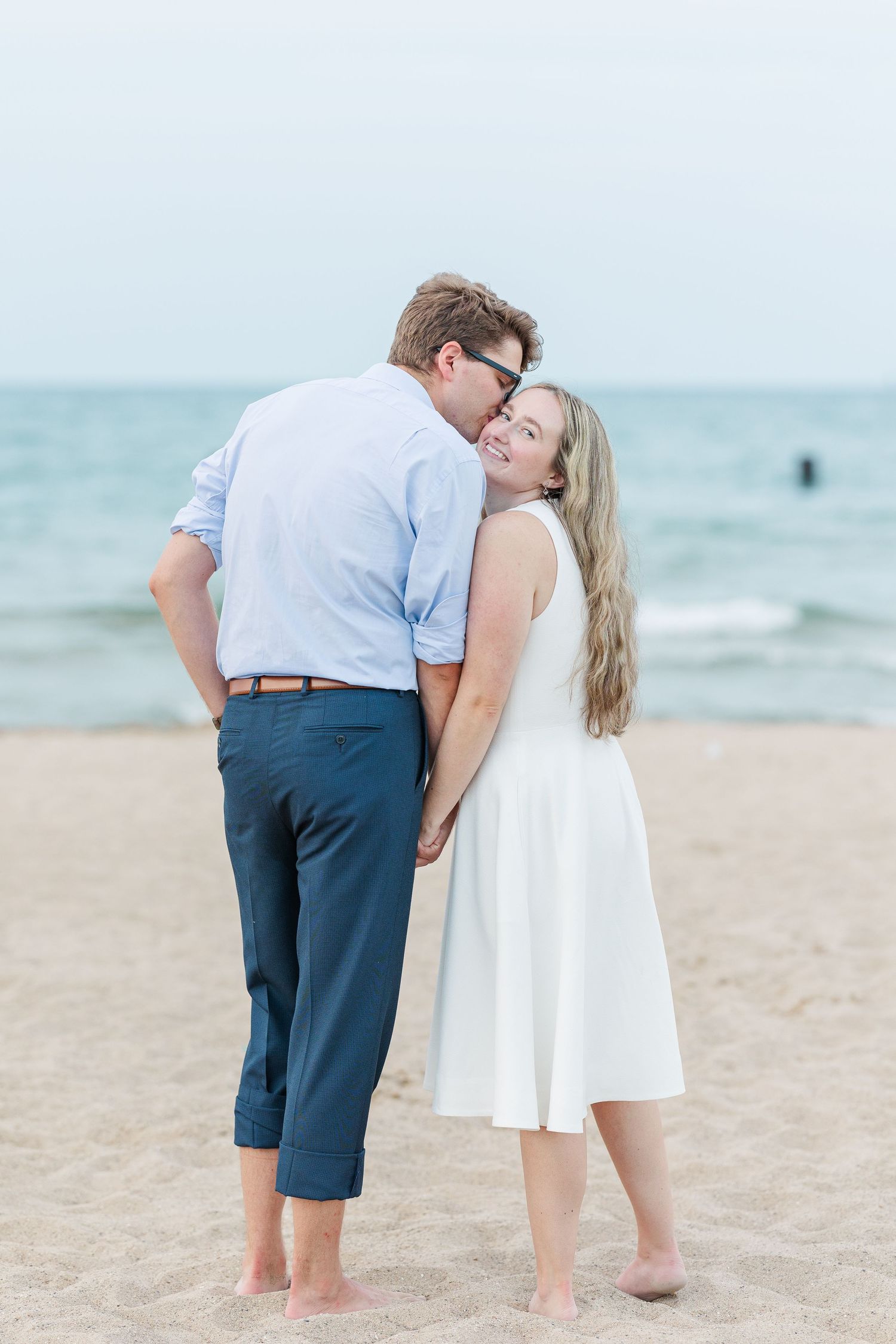 Elizabeth and Joe walking hand-in-hand along North Avenue Beach, with gentle waves and a soft sunset in the background