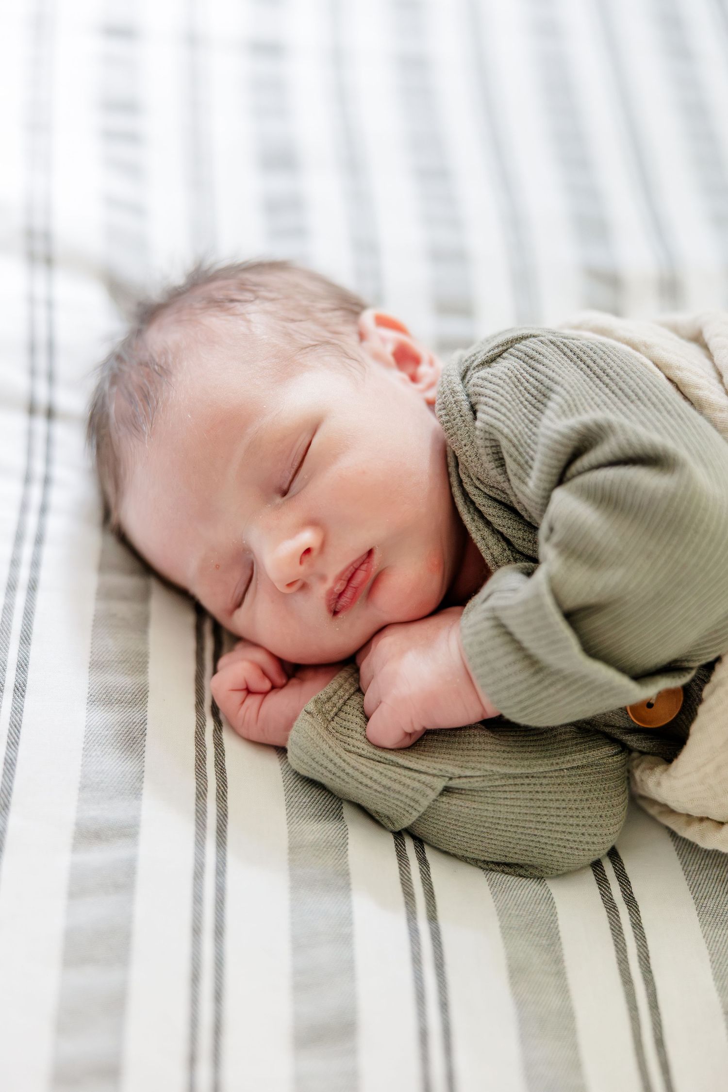 Peaceful newborn baby sleeping in green ribbed outfit on striped blanket in soft natural light.