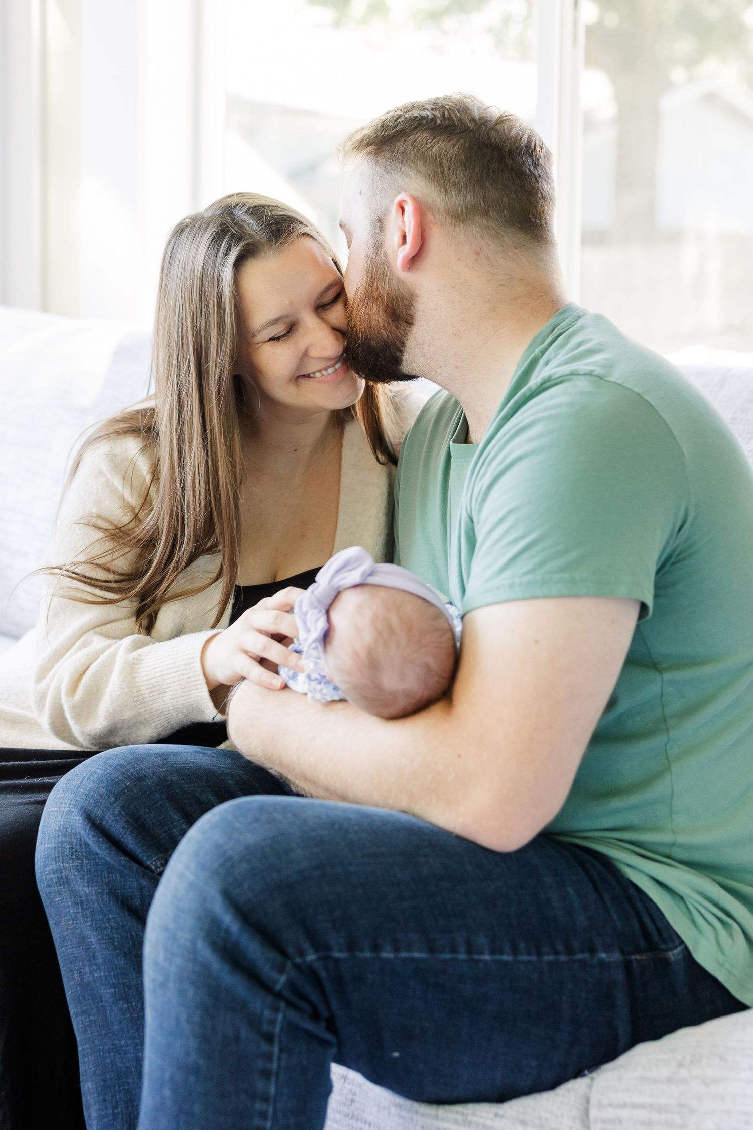 Happy couple sitting on couch sharing a tender moment while cradling their newborn baby together.