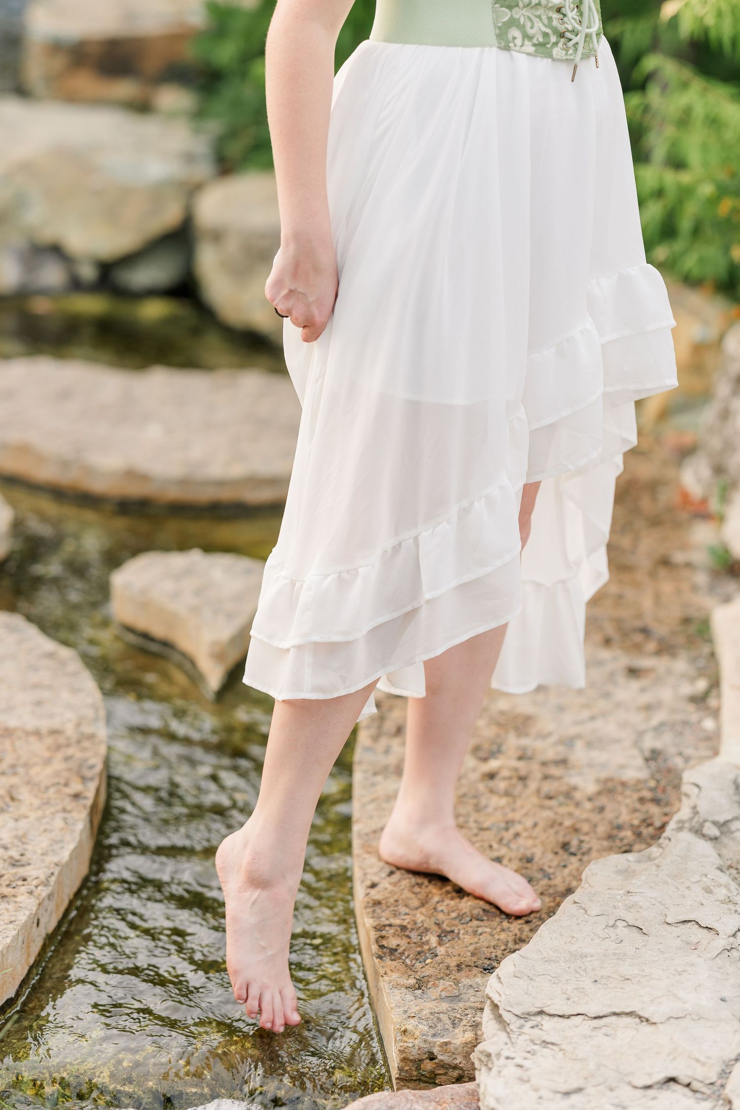 Detail of Samantha’s white dress and bare feet on garden rocks during her artistic senior portraits.