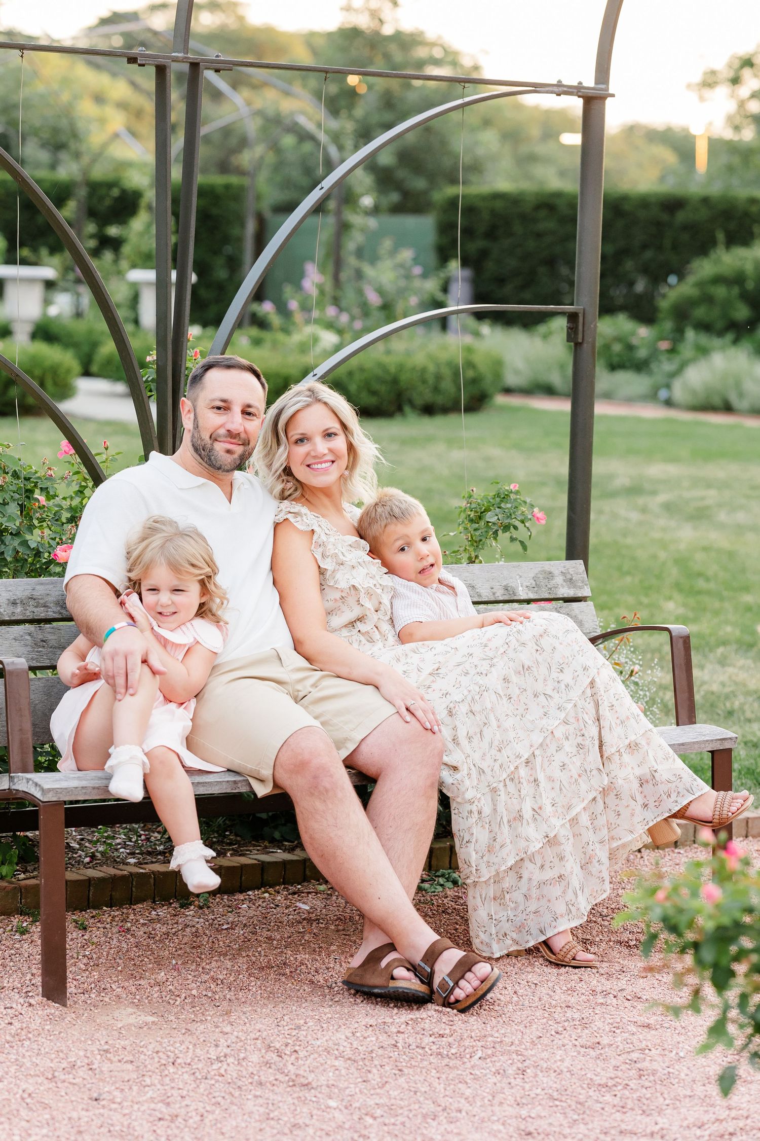 Family of four sitting together on a garden bench under a metal arbor at sunset.