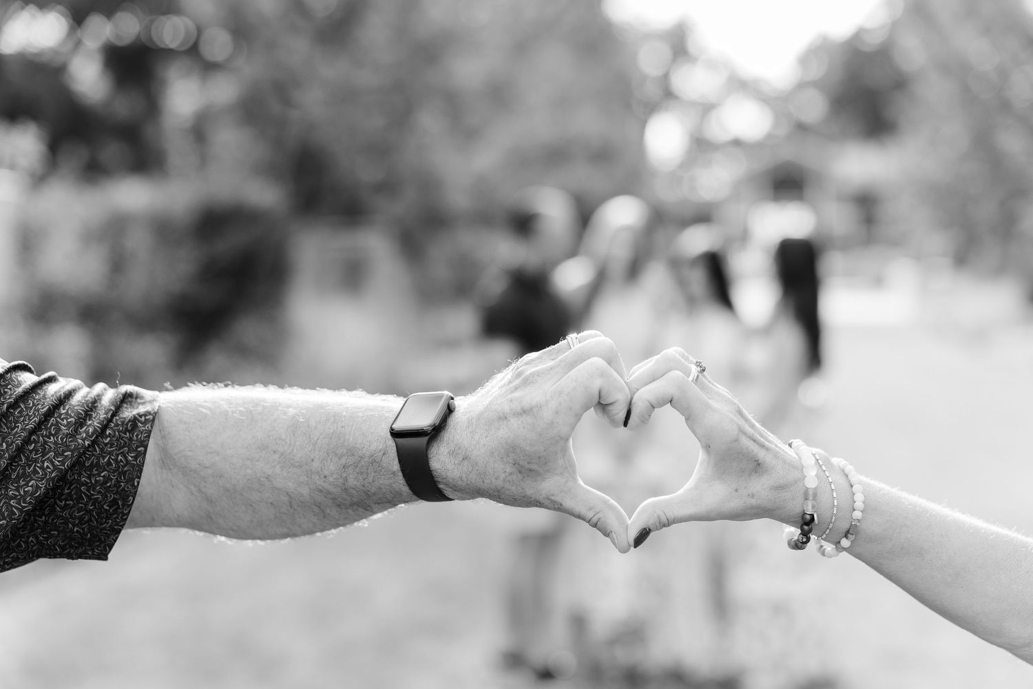 Black and white photo of a couple making a heart shape with their hands outdoors.