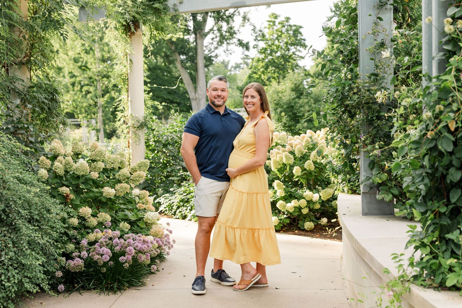 Smiling couple embracing under a pergola surrounded by blooming flowers.