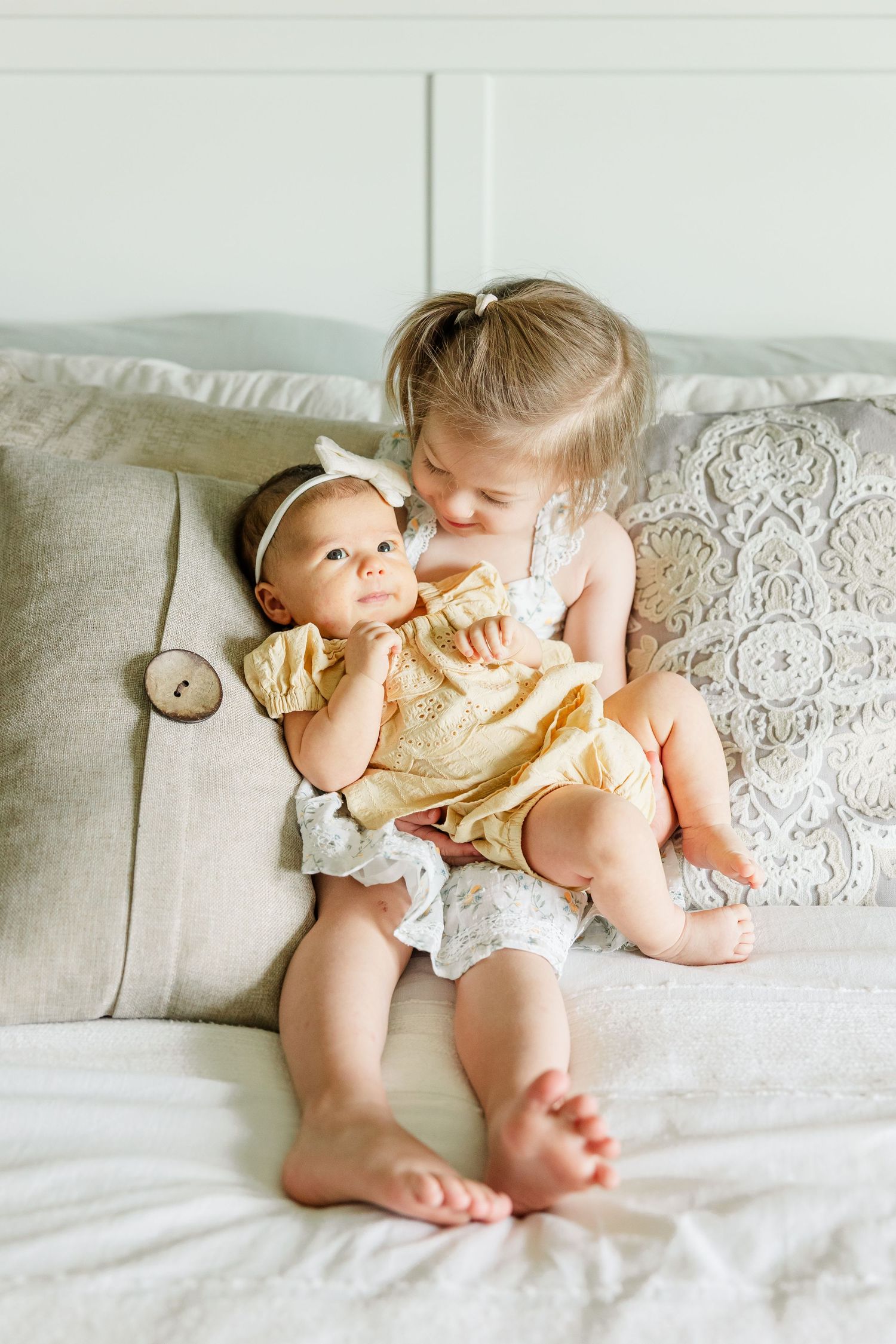 Big sister holding newborn baby girl on the bed during a sweet in-home lifestyle newborn session