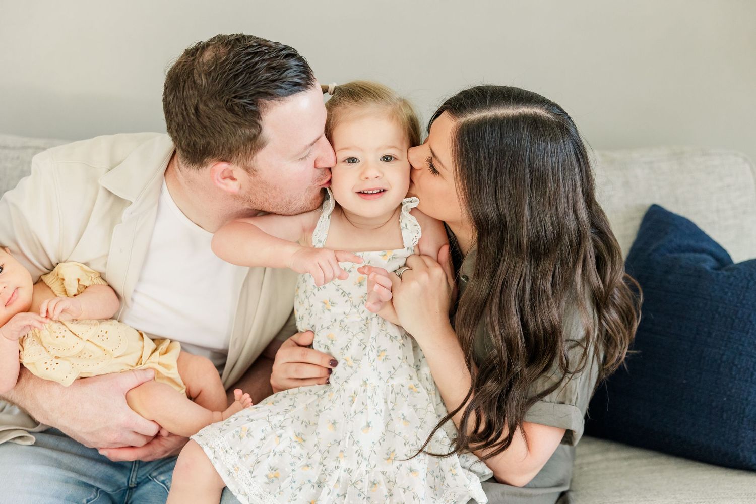 Parents kissing big sister while baby girl sleeps nearby during a lifestyle newborn session at home