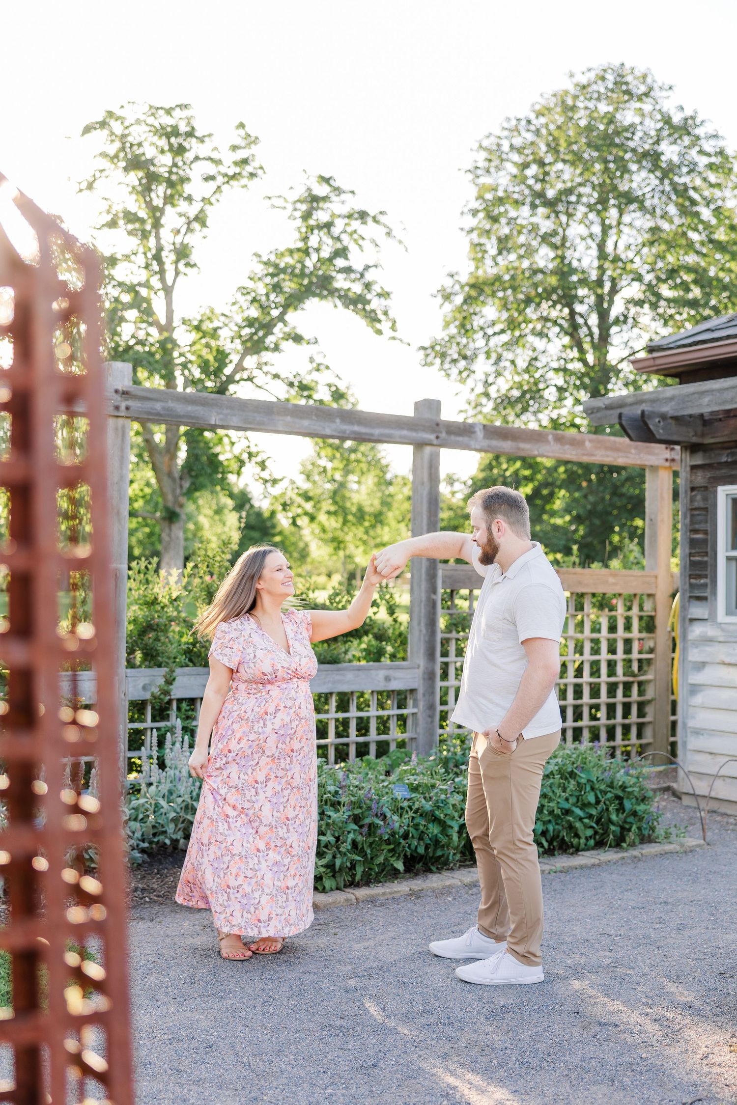 Parents-to-be holding hands and walking under a trellis during a Cantigny maternity session in Wheaton