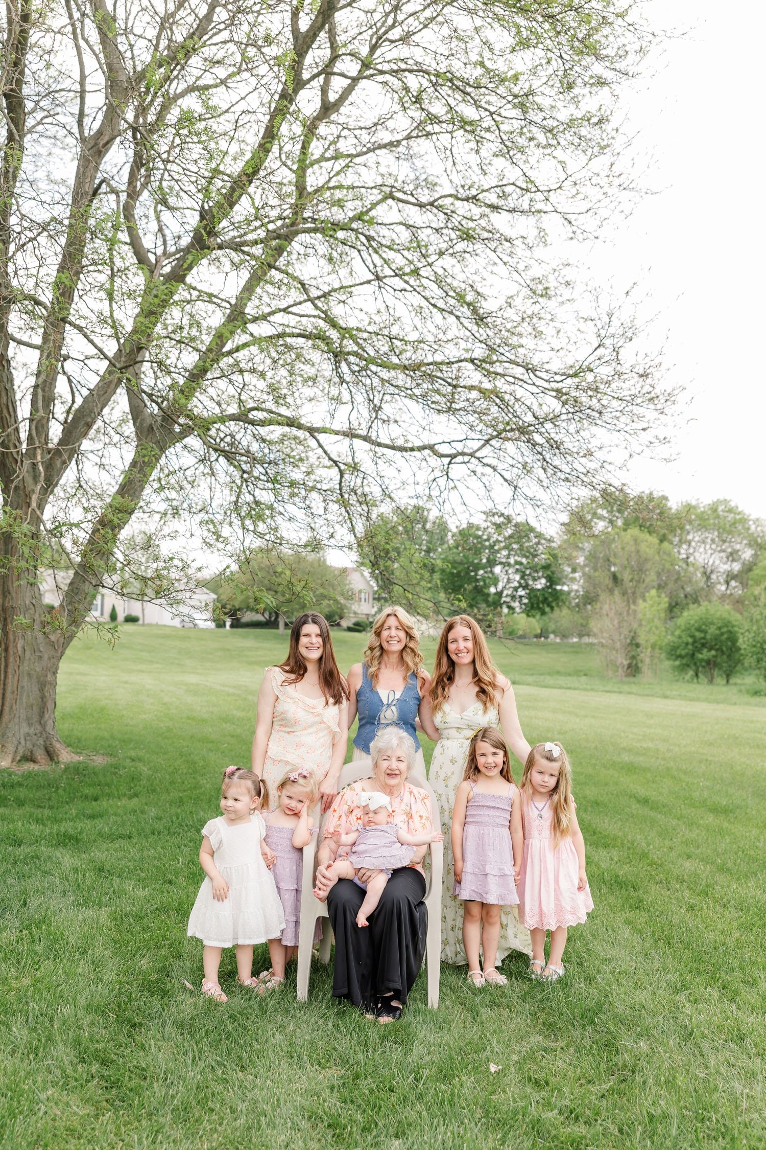 Multi-generational family portrait with grandmother, three adult women, and four young girls under a tree.