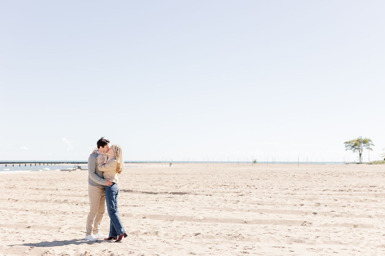 Romantic couple kissing on a serene sandy beach under a clear blue sky.