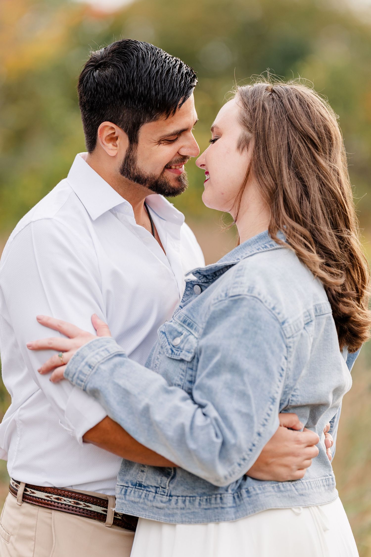 Close-up of a happy couple embracing and almost touching noses, the woman in a denim jacket and the man in a white shirt.