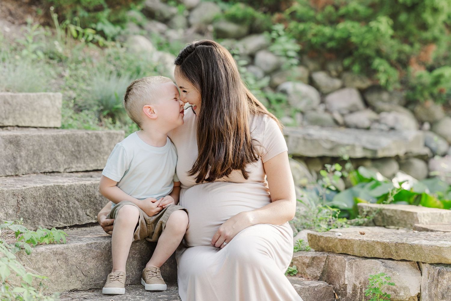 A romantic couple sits intimately on stone steps in a lush garden setting for engagement photos.
