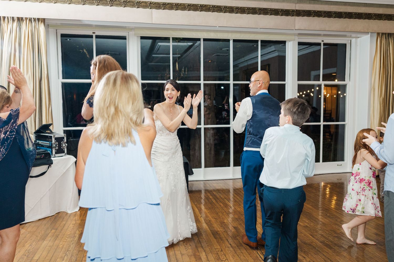 Wedding guests enjoying themselves on a dance floor with a bride visible in the background.