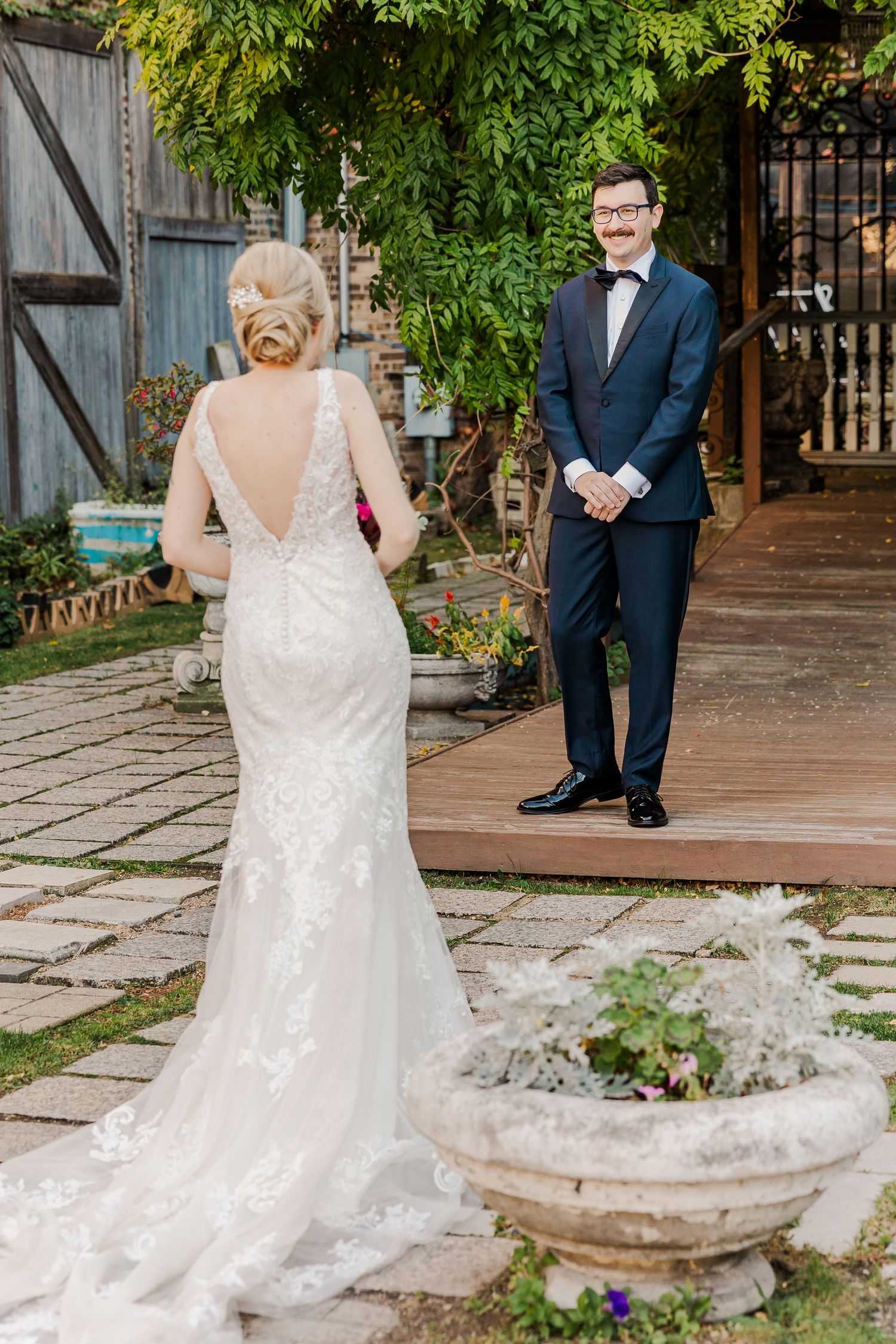 Couple's first look moment in lush garden setting with bride in backless gown and groom in tuxedo.