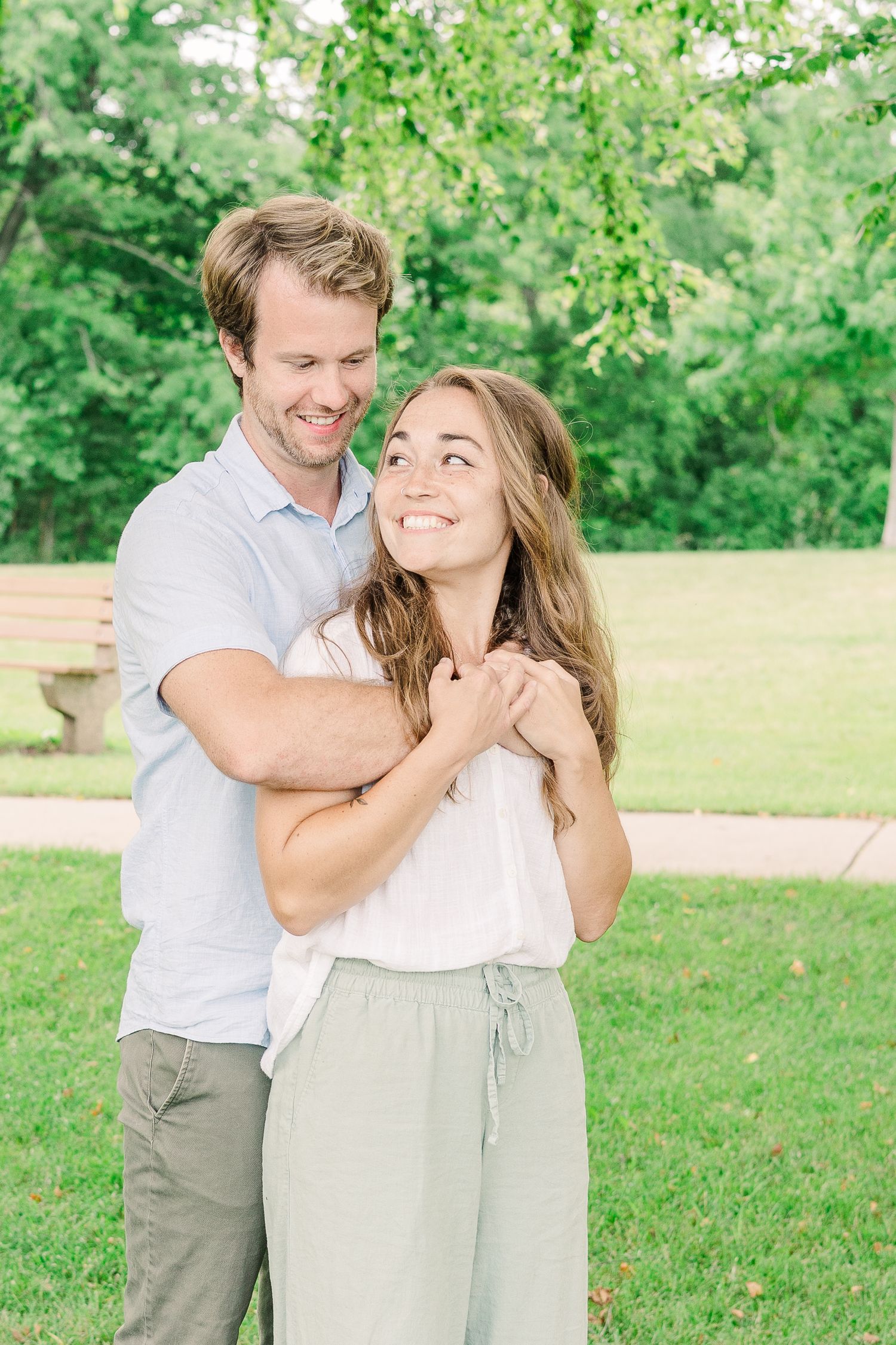 A romantic couple embraces outdoors while sharing a tender moment in a lush green park setting.