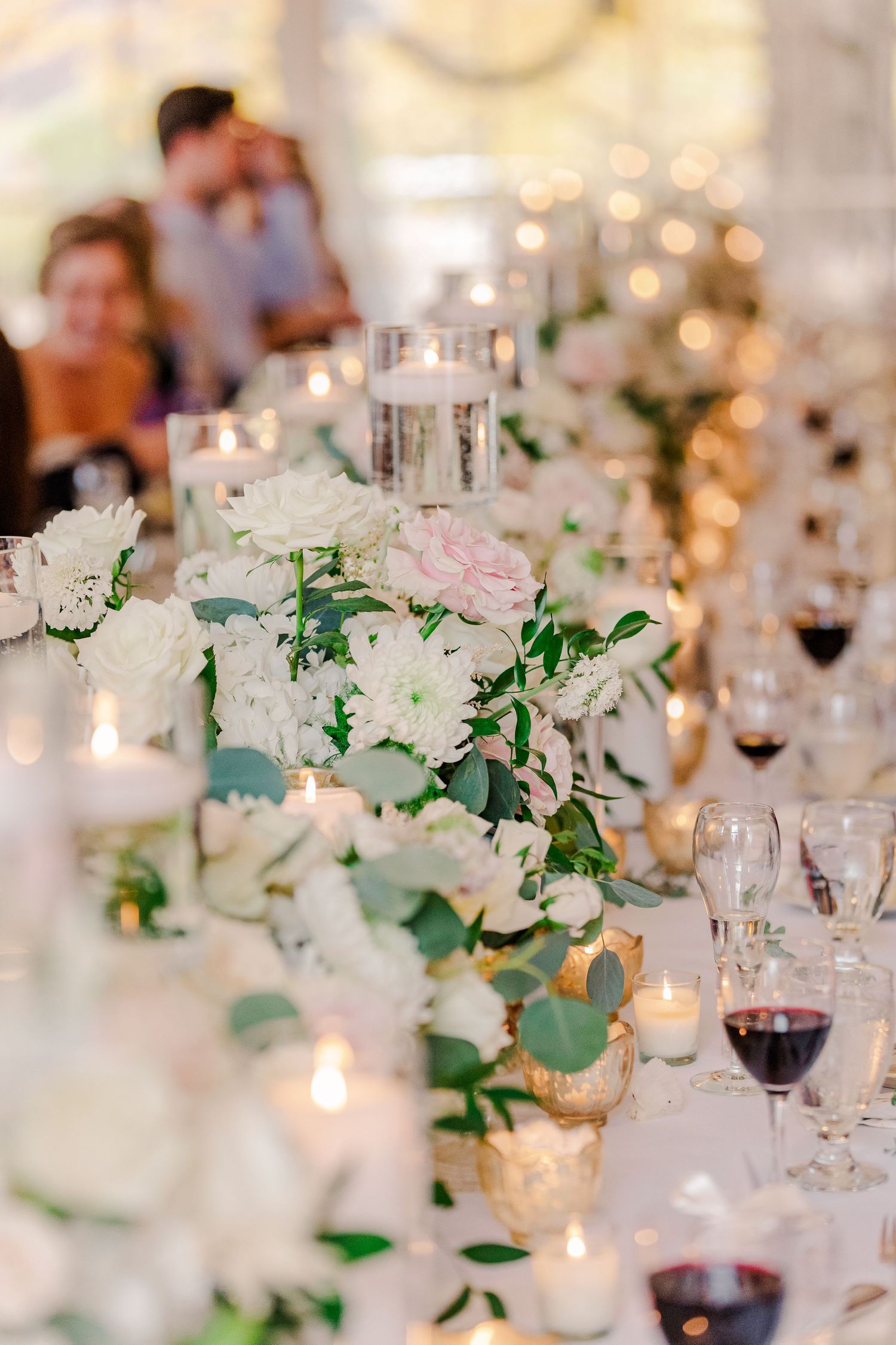 Elegant table setting with white flowers, greenery and candles at wedding reception.