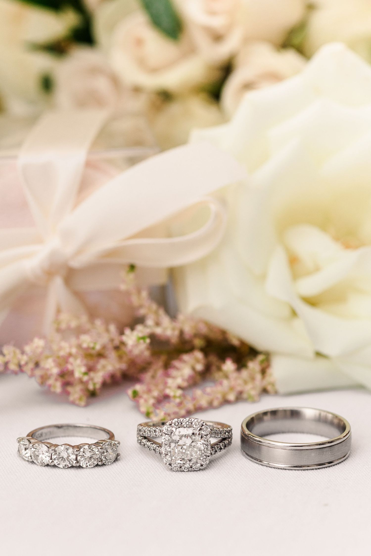 Three wedding rings displayed with white roses and pink floral accents.