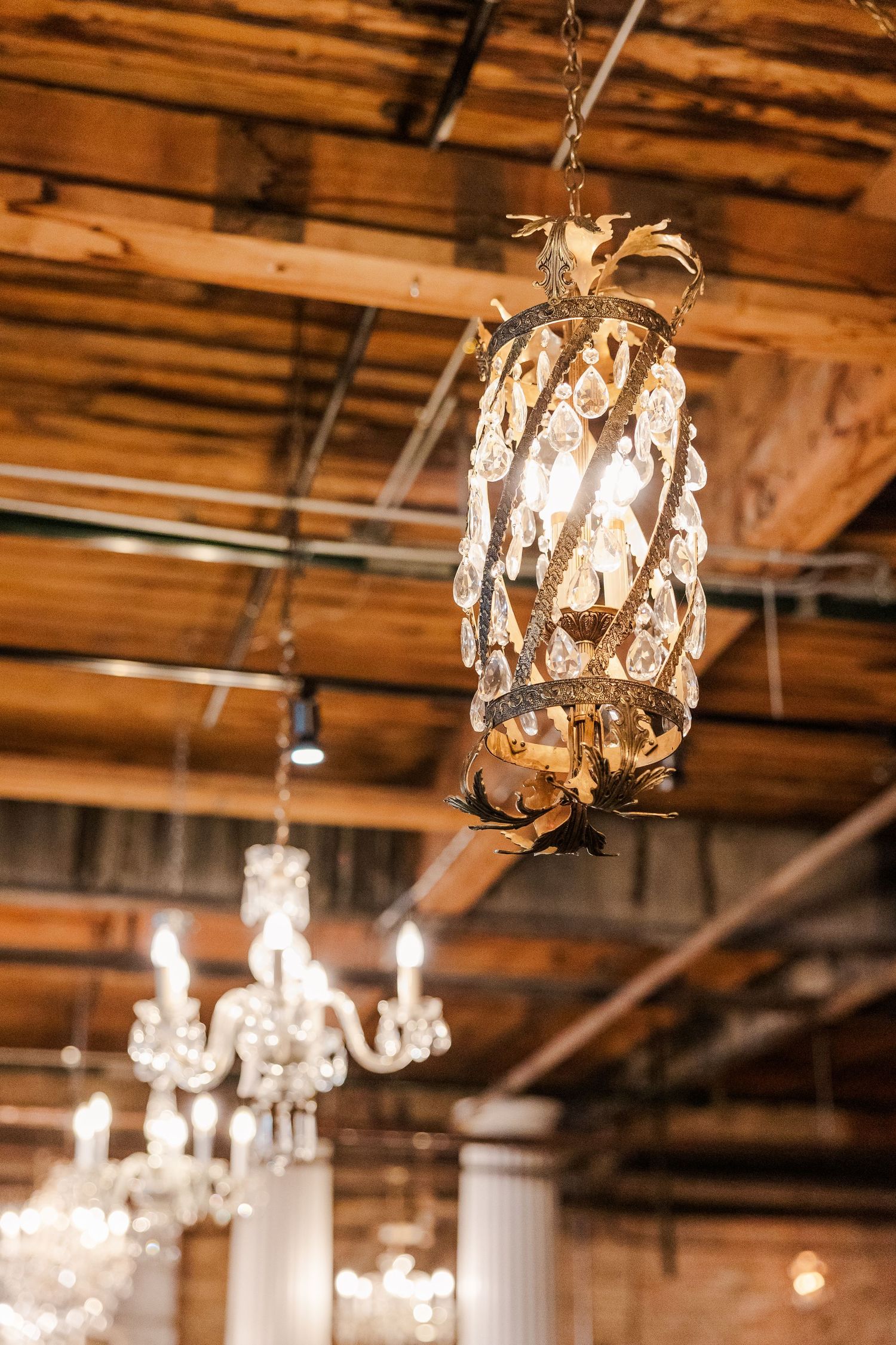 A close-up of an ornate crystal chandelier with warm lighting against wooden ceiling beams.