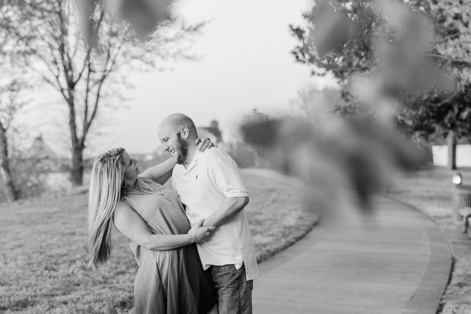 A black and white portrait of a couple sharing an intimate moment outdoors on a path.