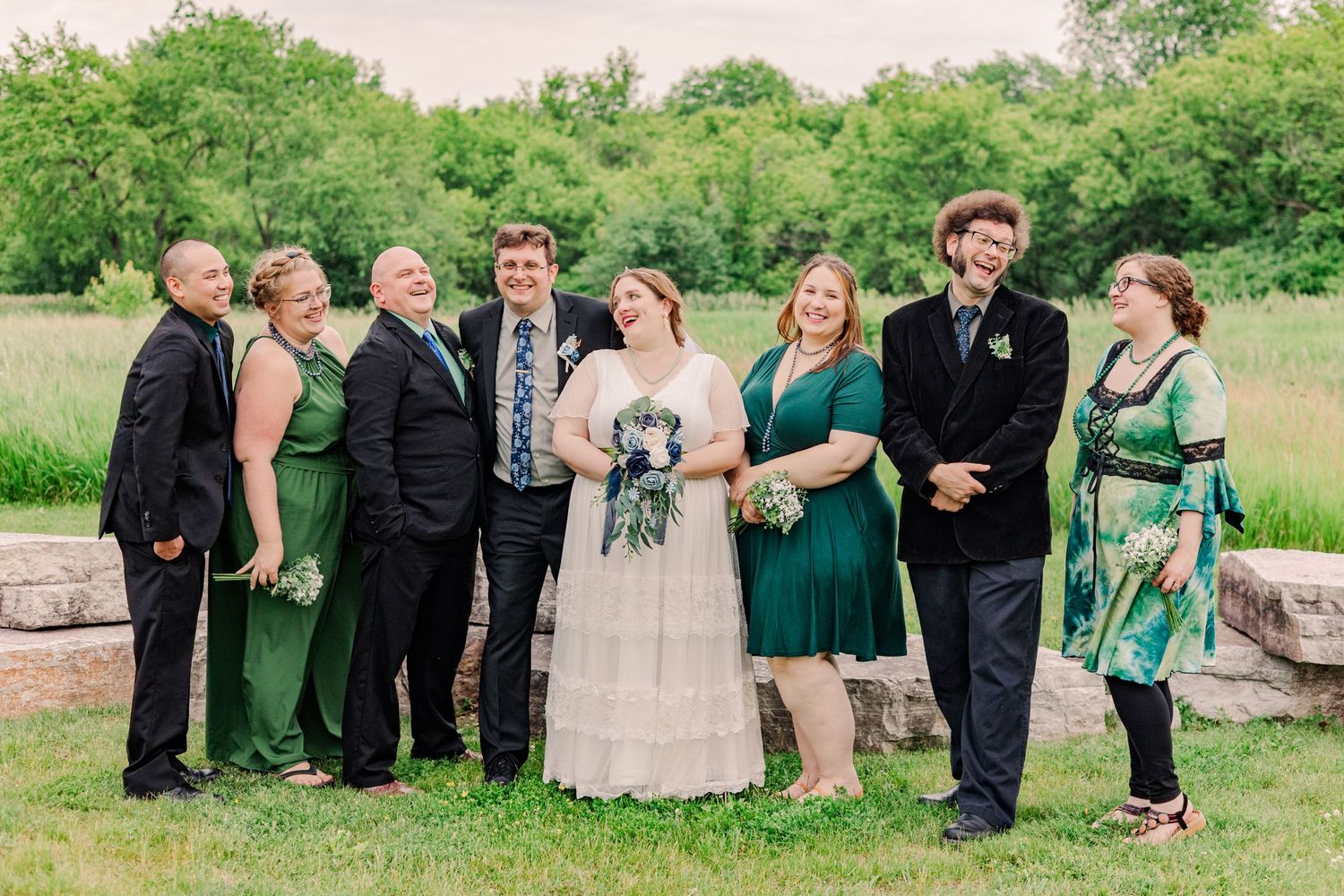 Wedding party poses formally outdoors wearing coordinated green and black attire.