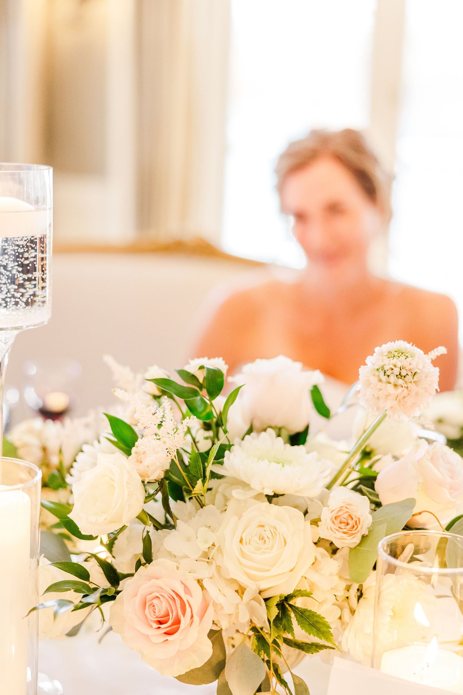 Elegant wedding reception table featuring white and blush floral centerpiece arrangements with roses and greenery.
