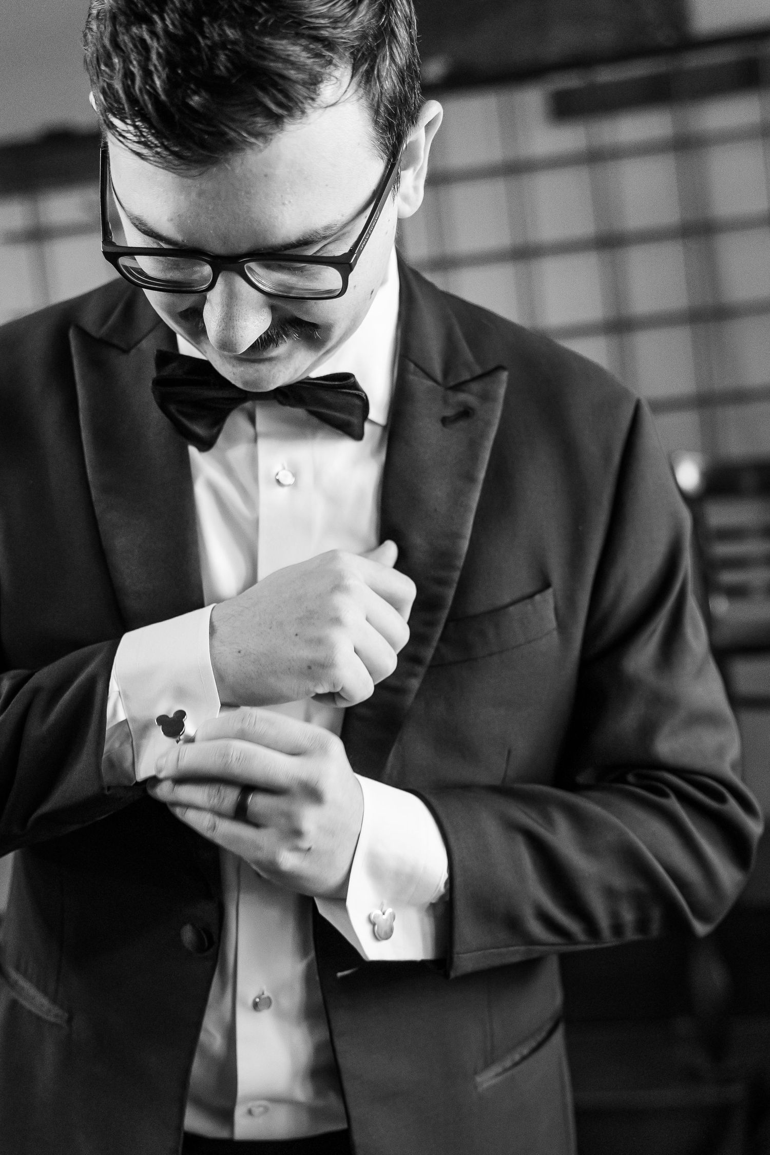A groom adjusts his cufflinks while wearing a classic black tuxedo and bow tie for a formal occasion.