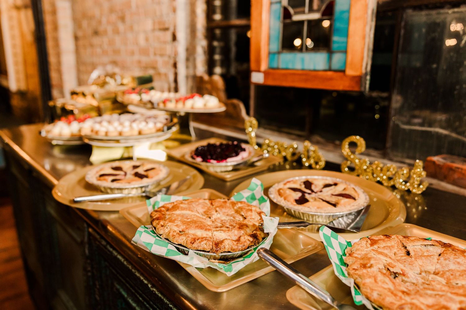 Array of homemade pies displayed on rustic wooden table at wedding reception.
