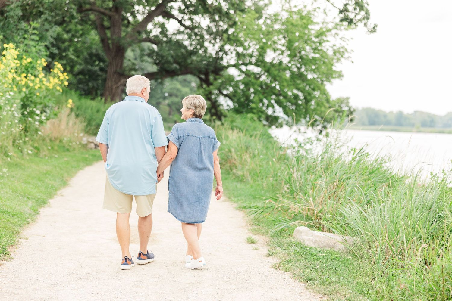 Senior couple taking a romantic walk along a lakeside path surrounded by greenery.