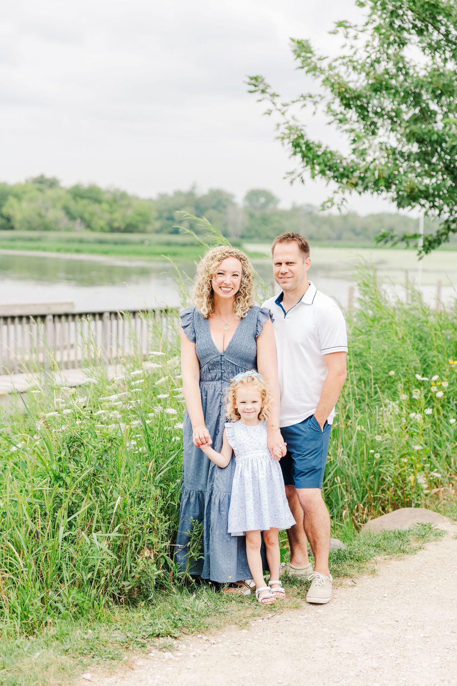 A sweet family portrait taken on a path beside a tranquil lake with lush greenery in the background.