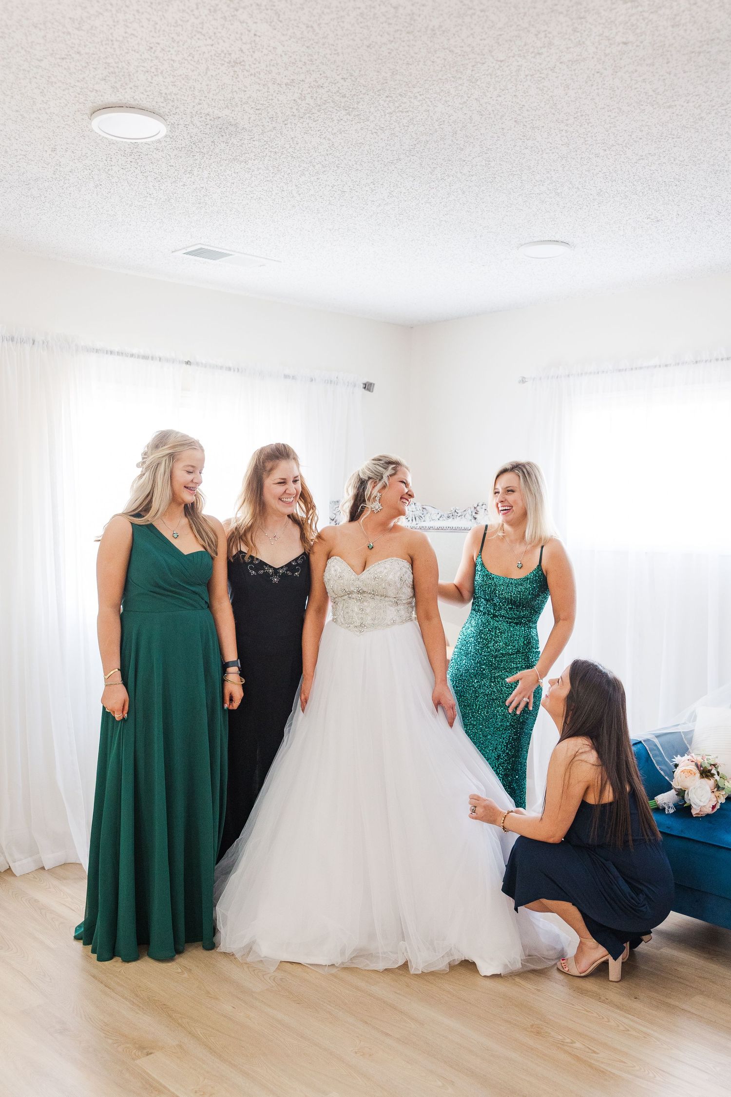 Wedding party in green and black dresses gathered around stunning white wedding gown.