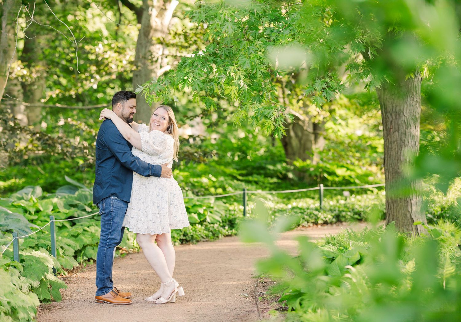 A sweet embrace captured on a sunlit garden pathway surrounded by greenery.