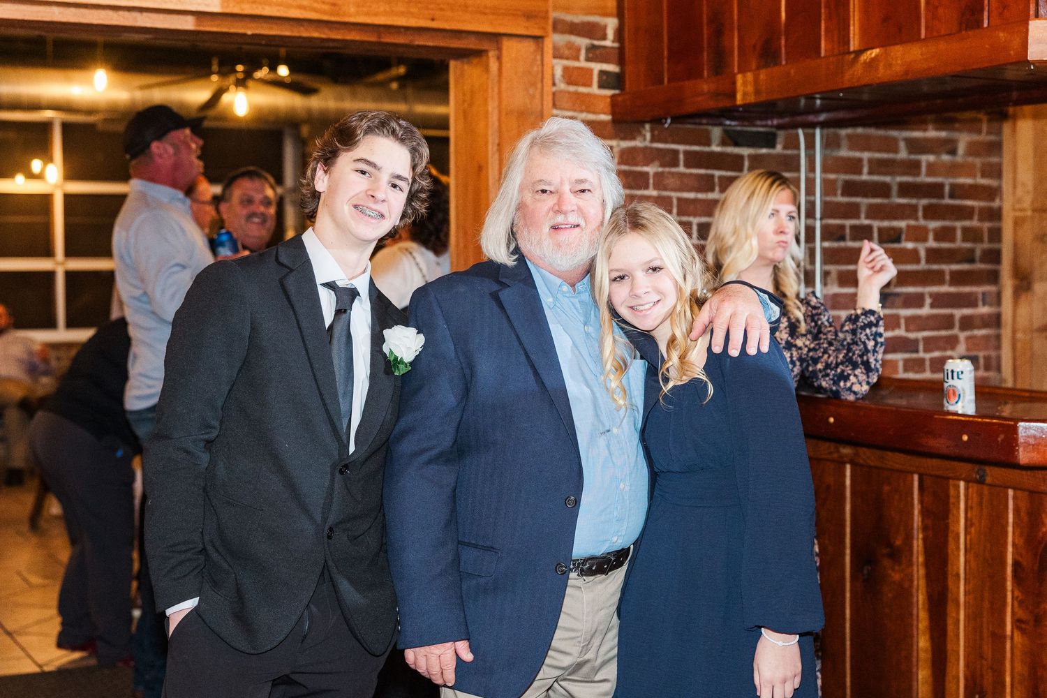Wedding guests pose together against a rustic brick wall backdrop at a reception venue.