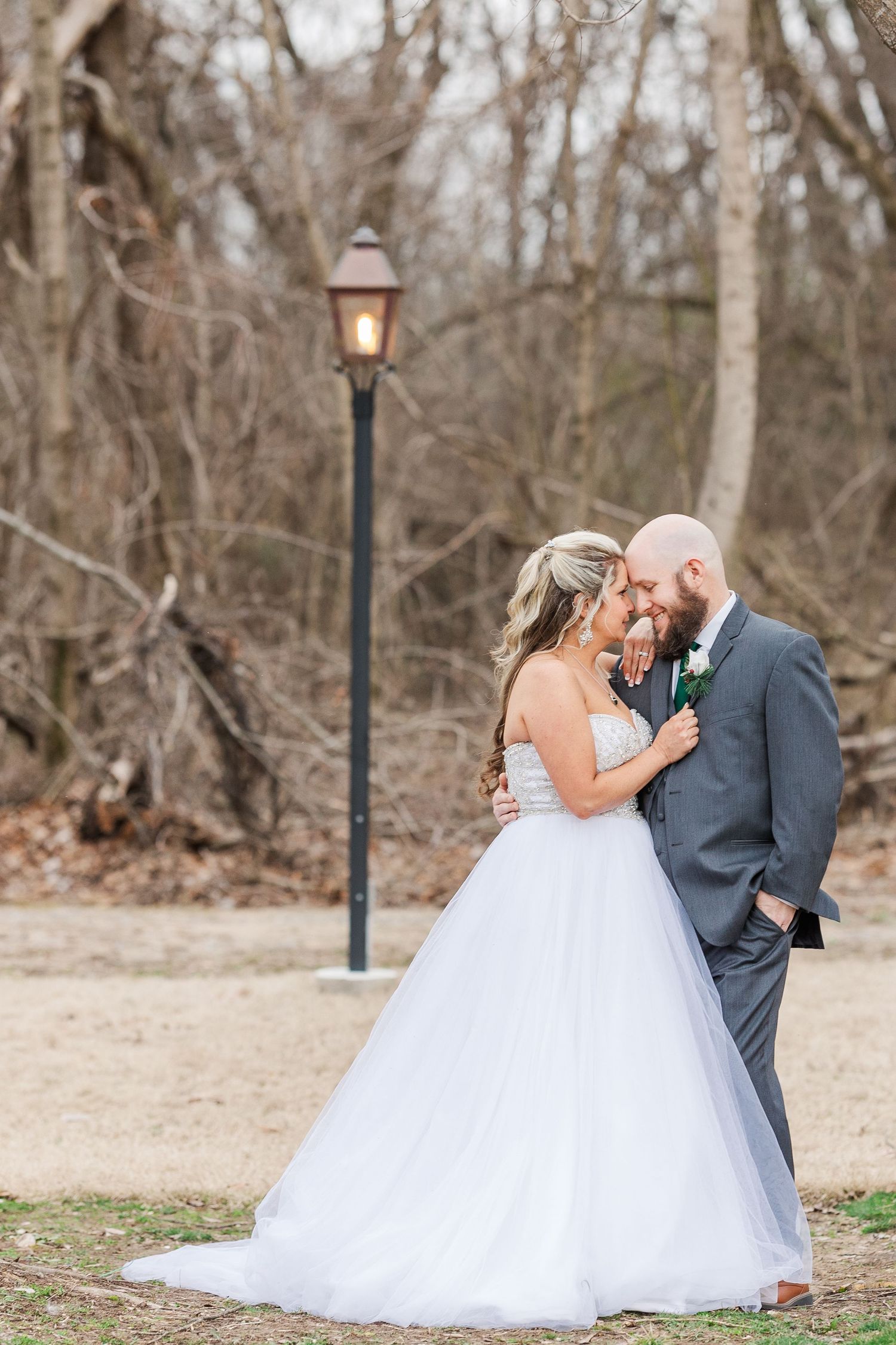 Elegant wedding couple poses by vintage lamp post in a serene park setting.