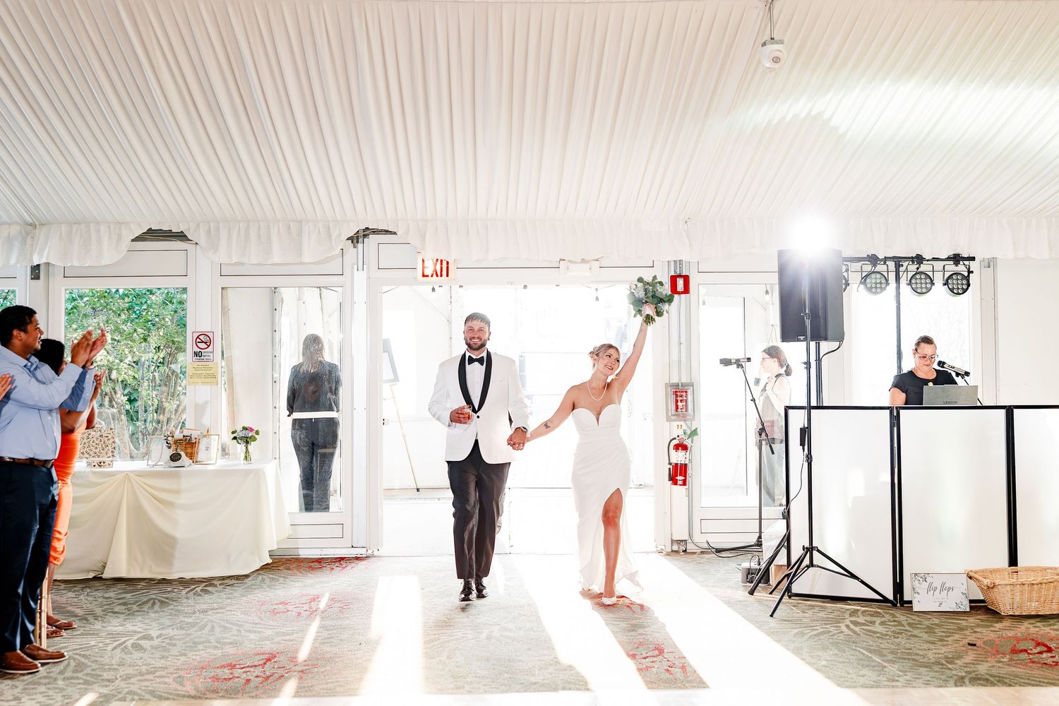 Bride and groom make a grand entrance into a bright white wedding reception venue as guests applaud.