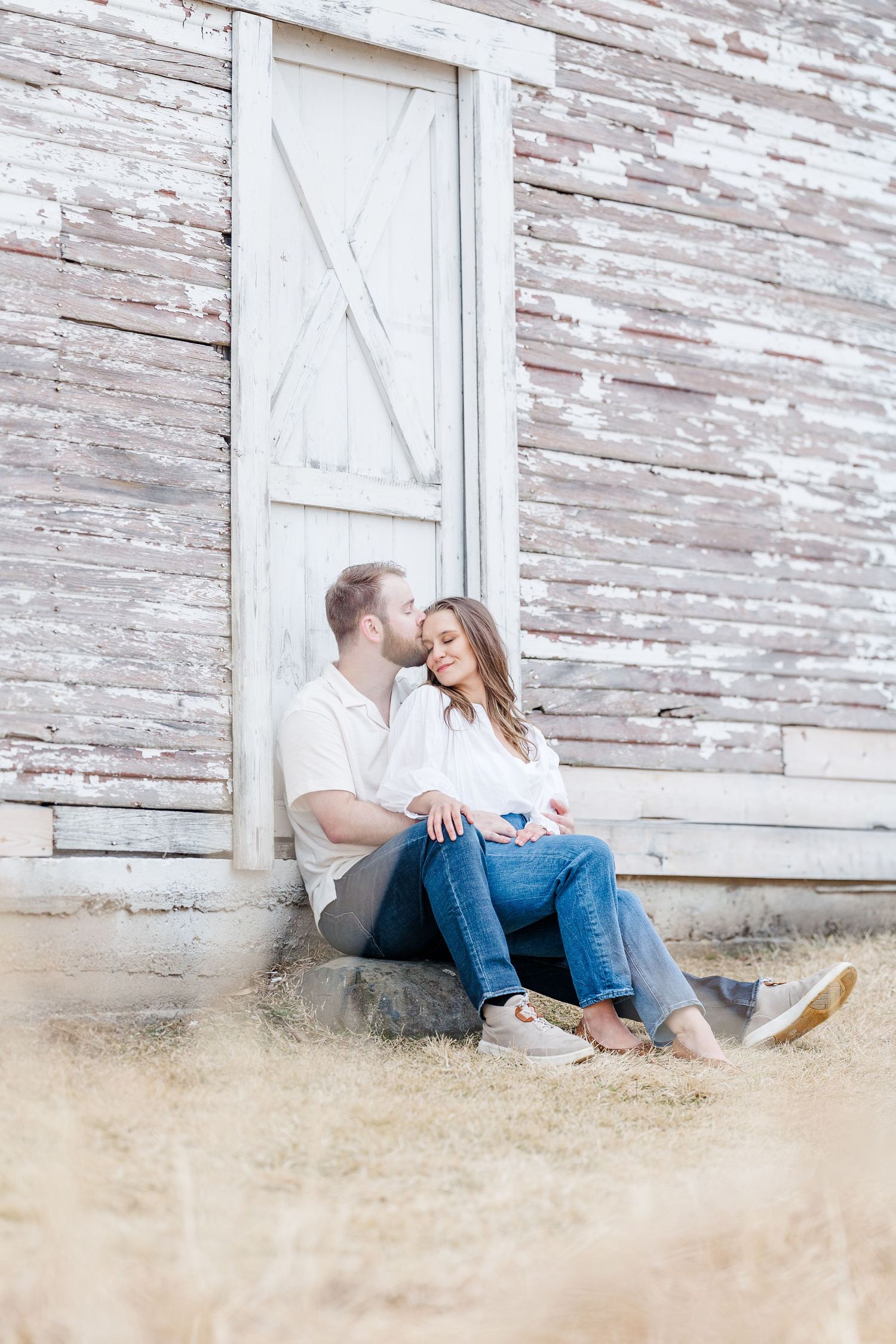 Couple sitting by barn door during pregnancy announcement photos in Cary, Illinois