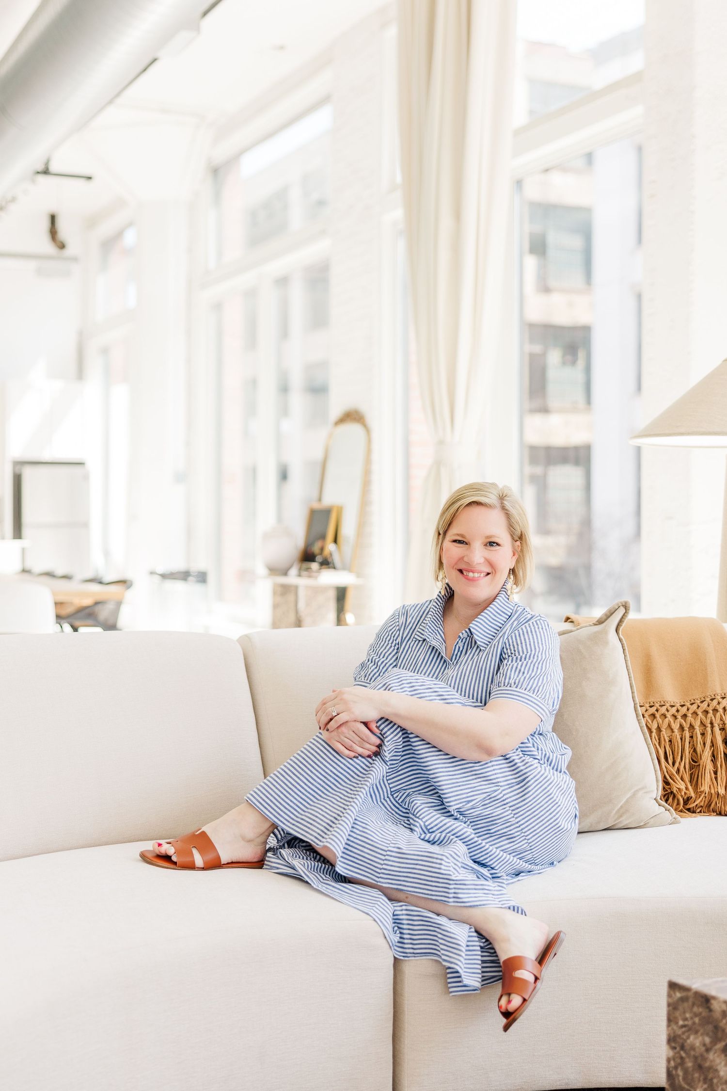 Cassie Lacina sitting on a cream sofa during a branding headshot session at The Studio Chicago in a bright, modern natural light studio
