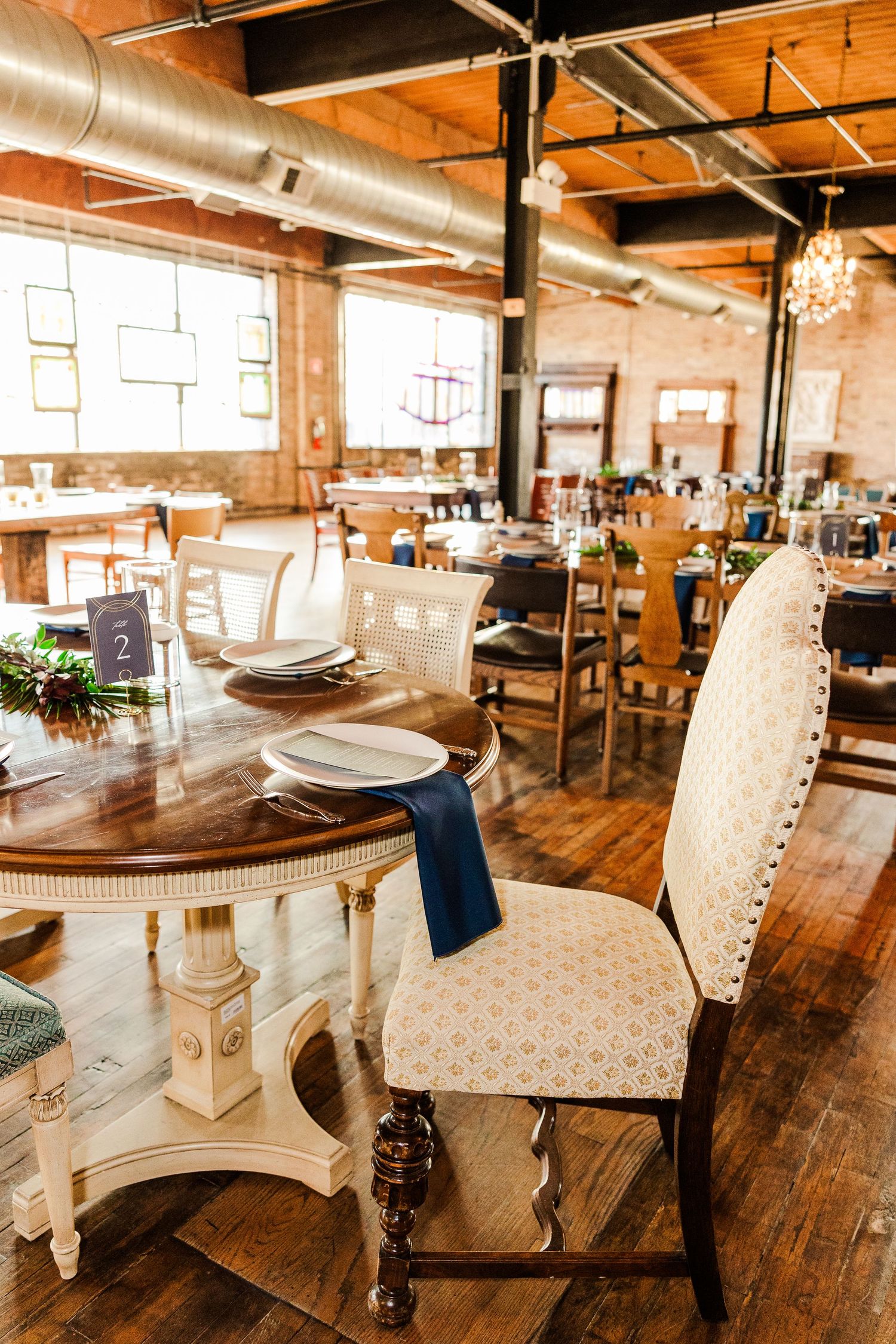 Elegant vintage dining room with ornate chairs, crystal chandeliers and exposed industrial ceiling.