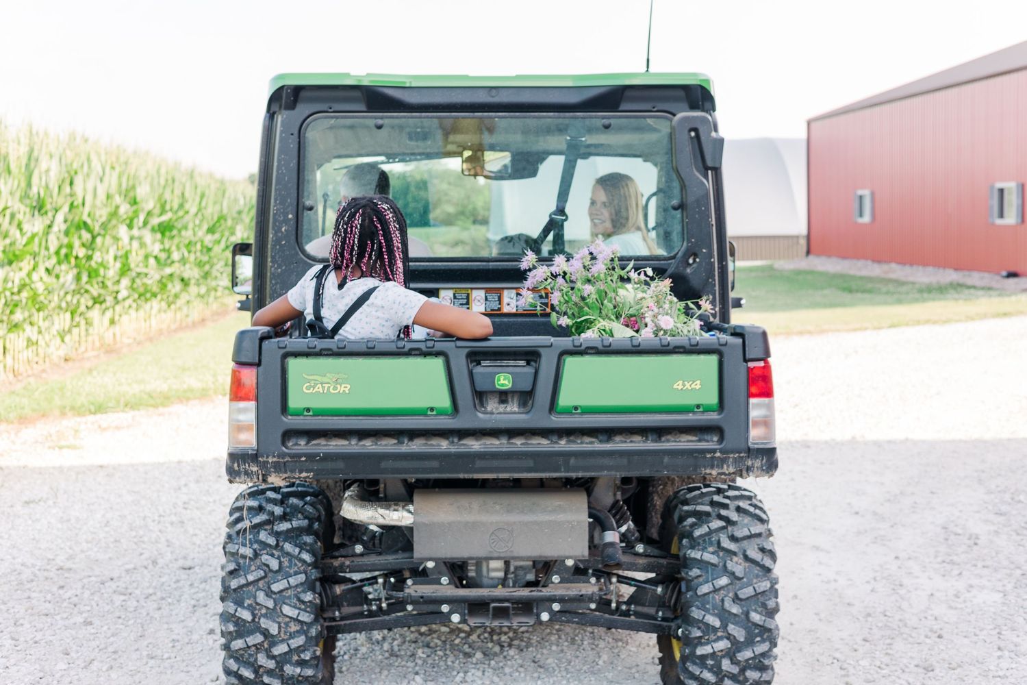 Back view of a green utility vehicle with gear loaded in the cargo area near a red barn.
