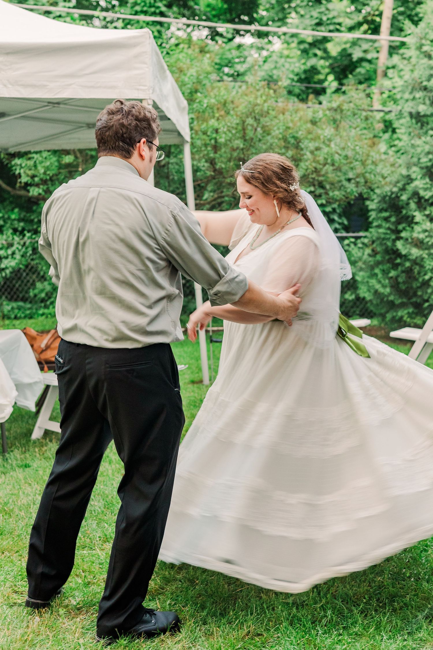 Couple dancing together outdoors under a white tent during their wedding celebration.