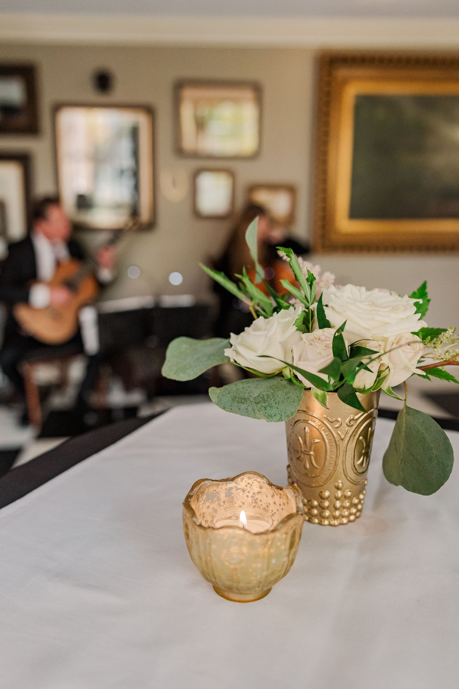 White roses and eucalyptus in gold vase with soft focus decor in background.